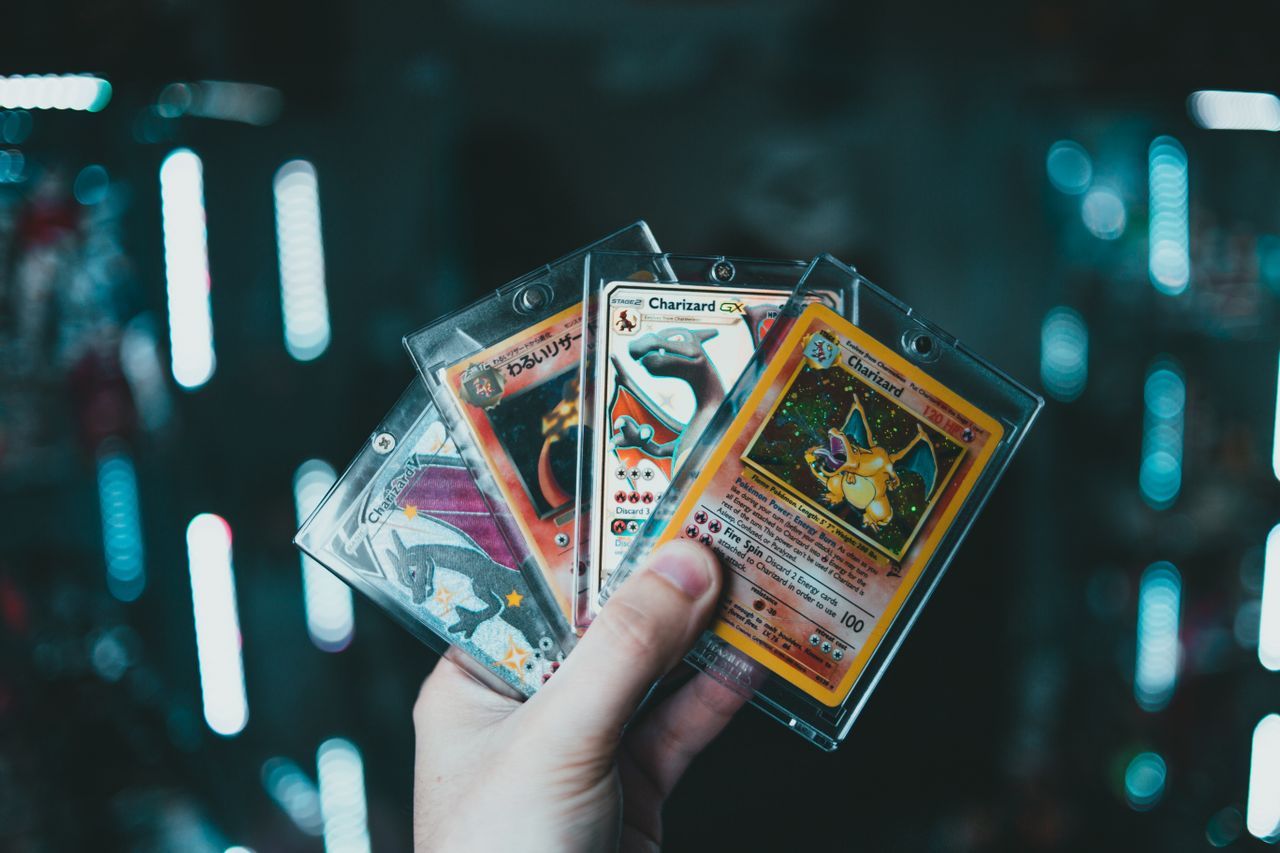 about-01 A hand holds collectible Charizard Pokemon cards with a blurred bokeh background. Perfect for trading card enthusiasts.